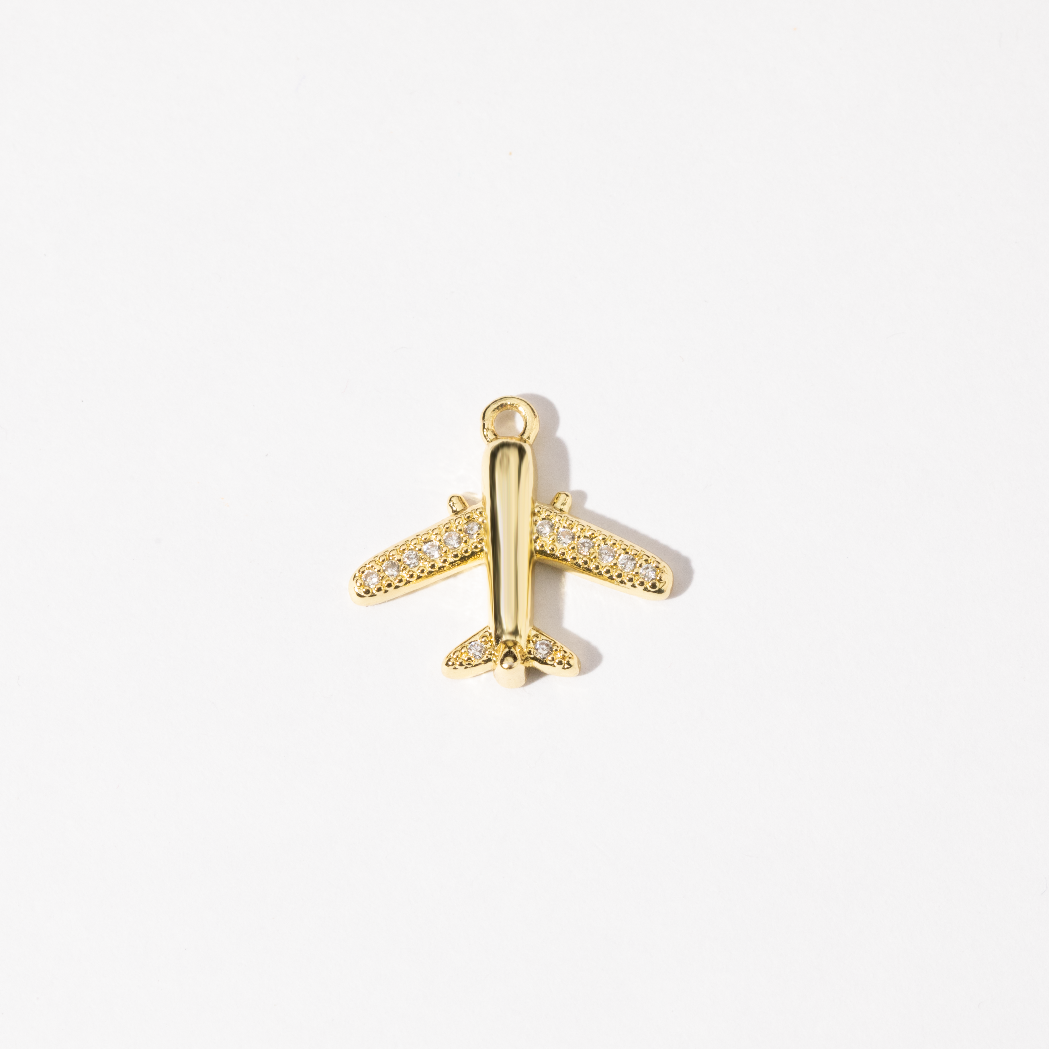 A gold-colored airplane-shaped charm with cubic zirconia stones adorning its body.
