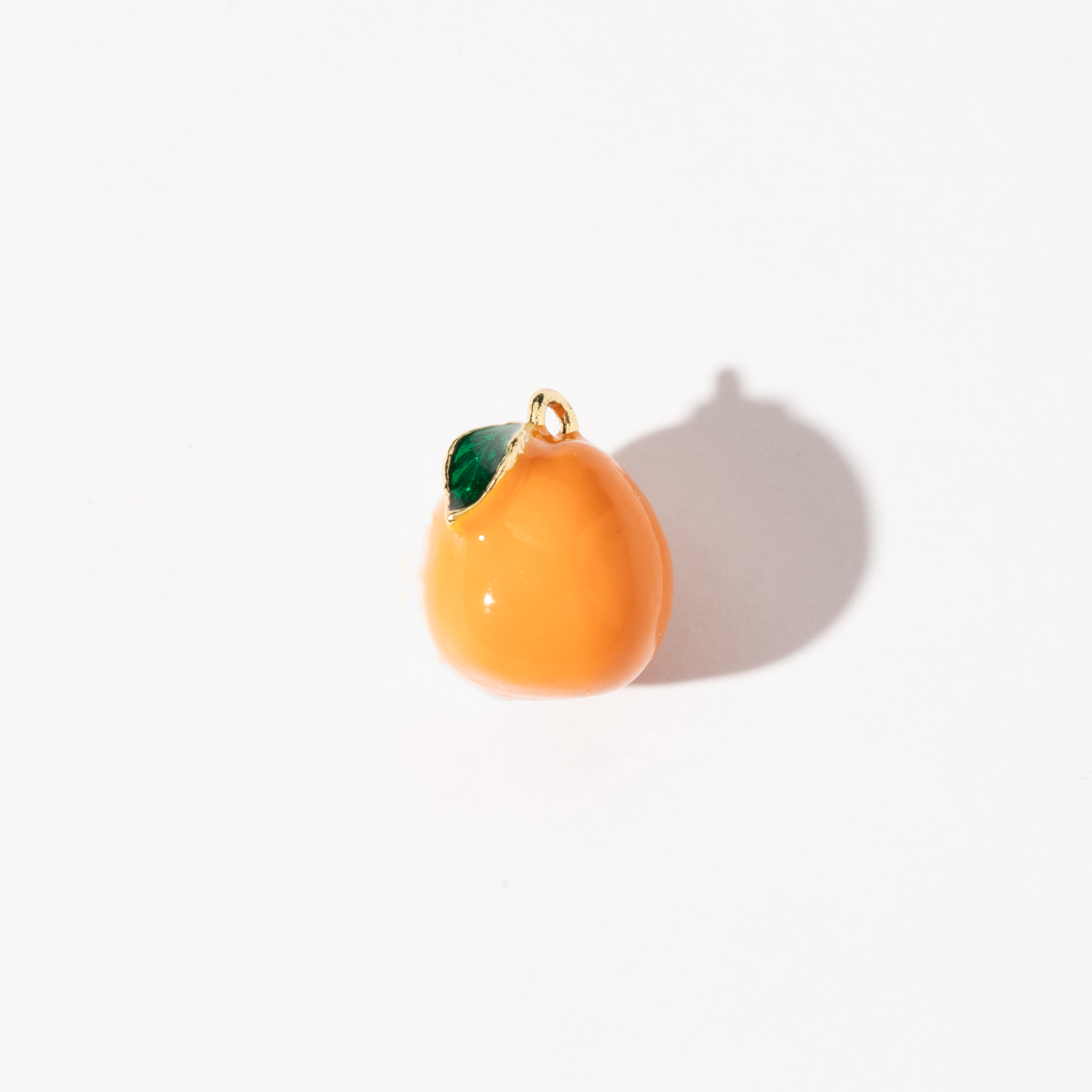 A gold-plated stainless steel charm in the shape of an orange with a green leaf detail, displayed against a white background.