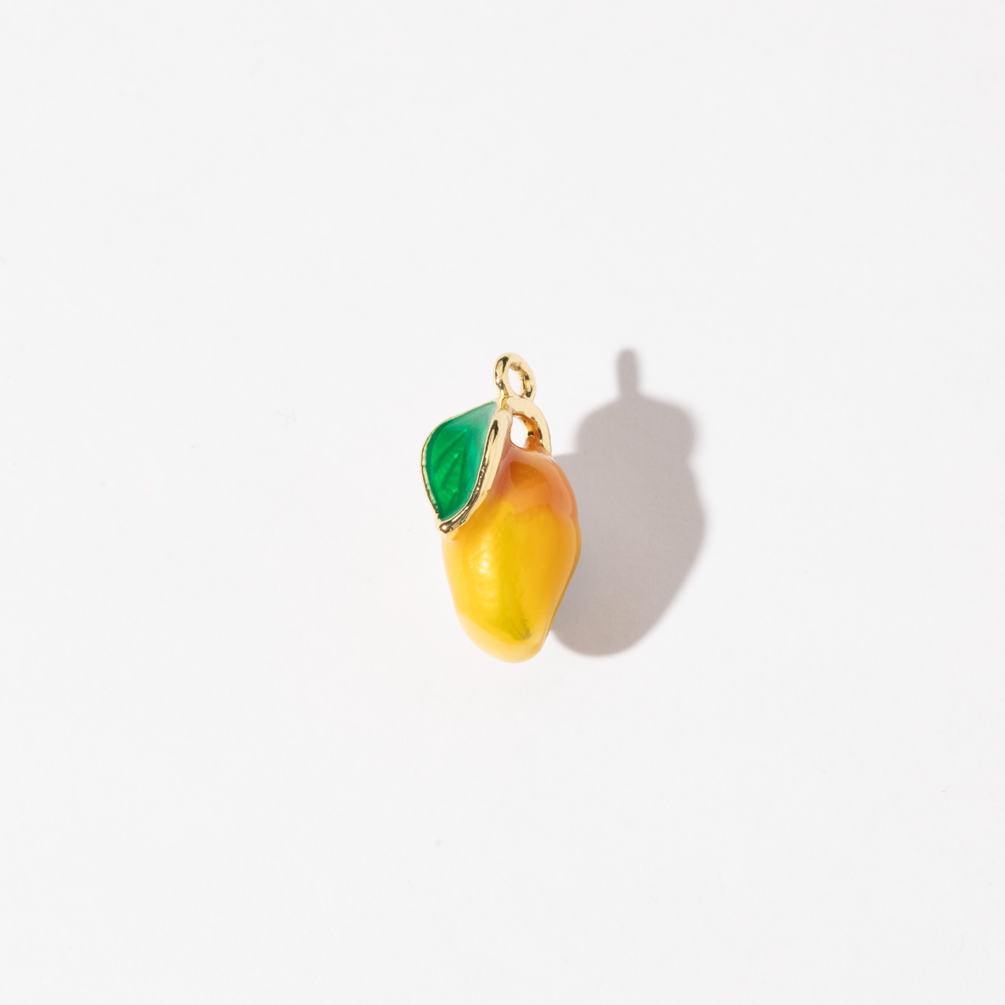 A gold-plated stainless steel charm in the shape of a mango with a green leaf, made with colored enamel.