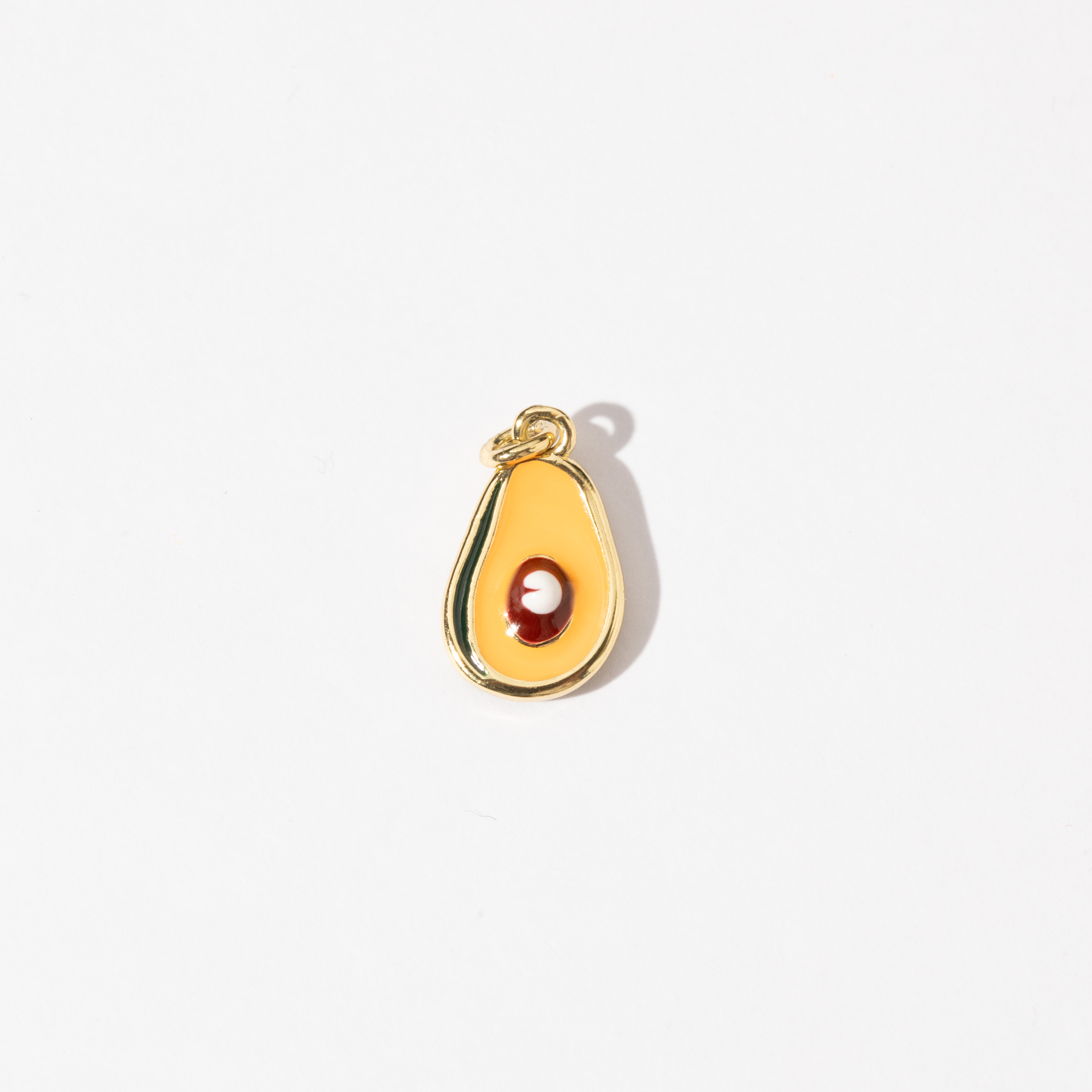 A gold-plated stainless steel charm in the shape of a half-avocado design with a polished seed at the center