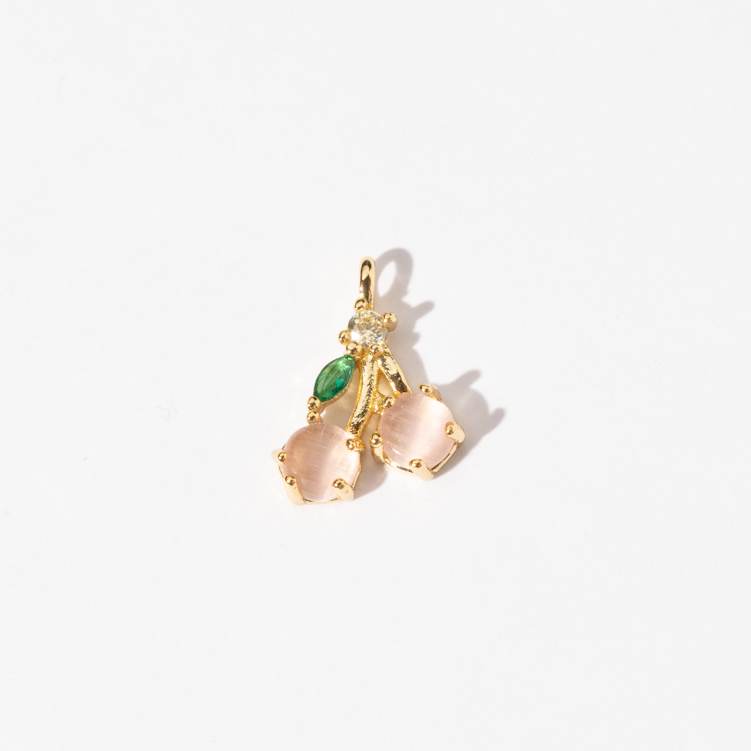 A gold-plated charm featuring a cherry design with pink stones and a small green gemstone accent.