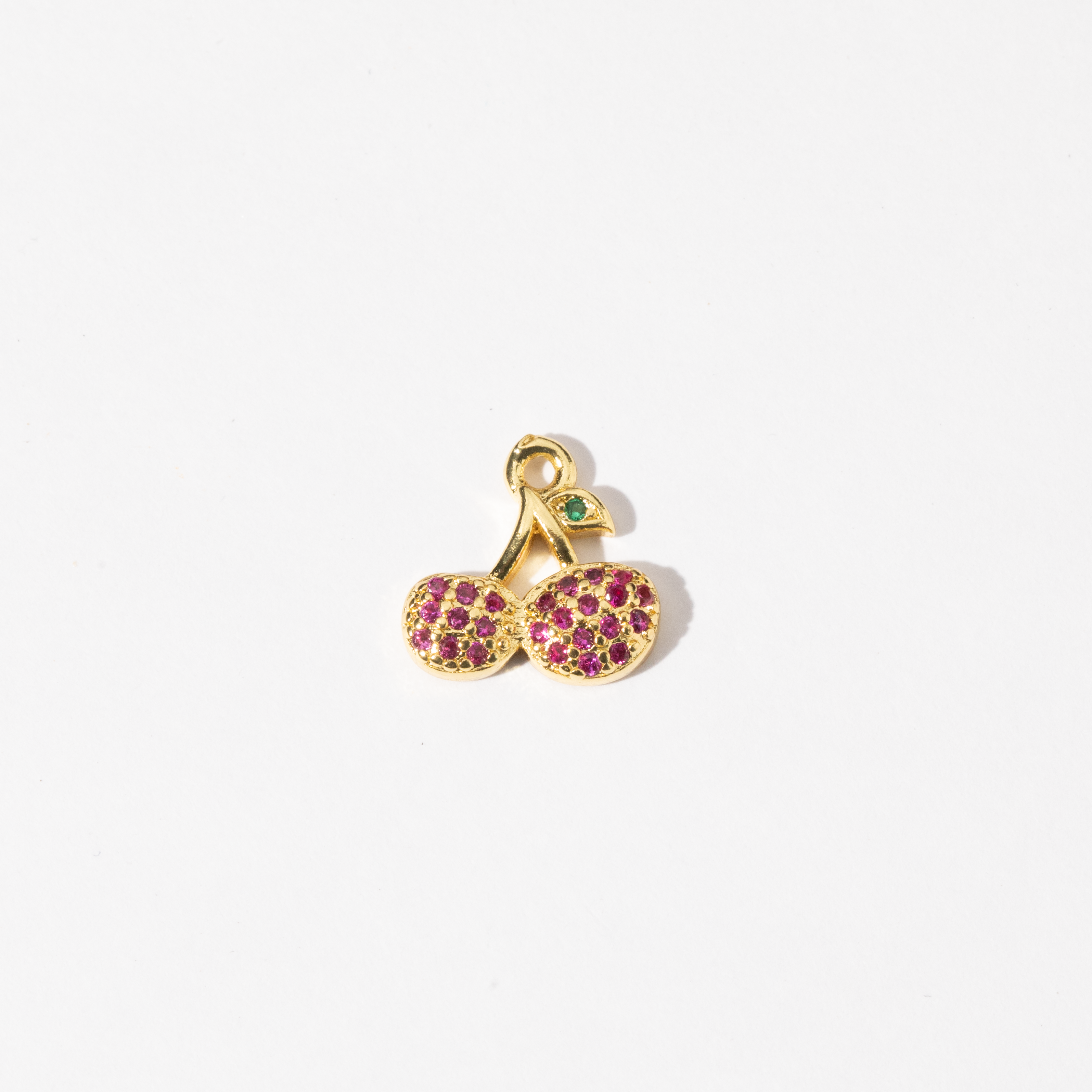 A custom made gold plated stainless steel charm in the shape of two cherries with red zirconia paving and a green gem leaf.