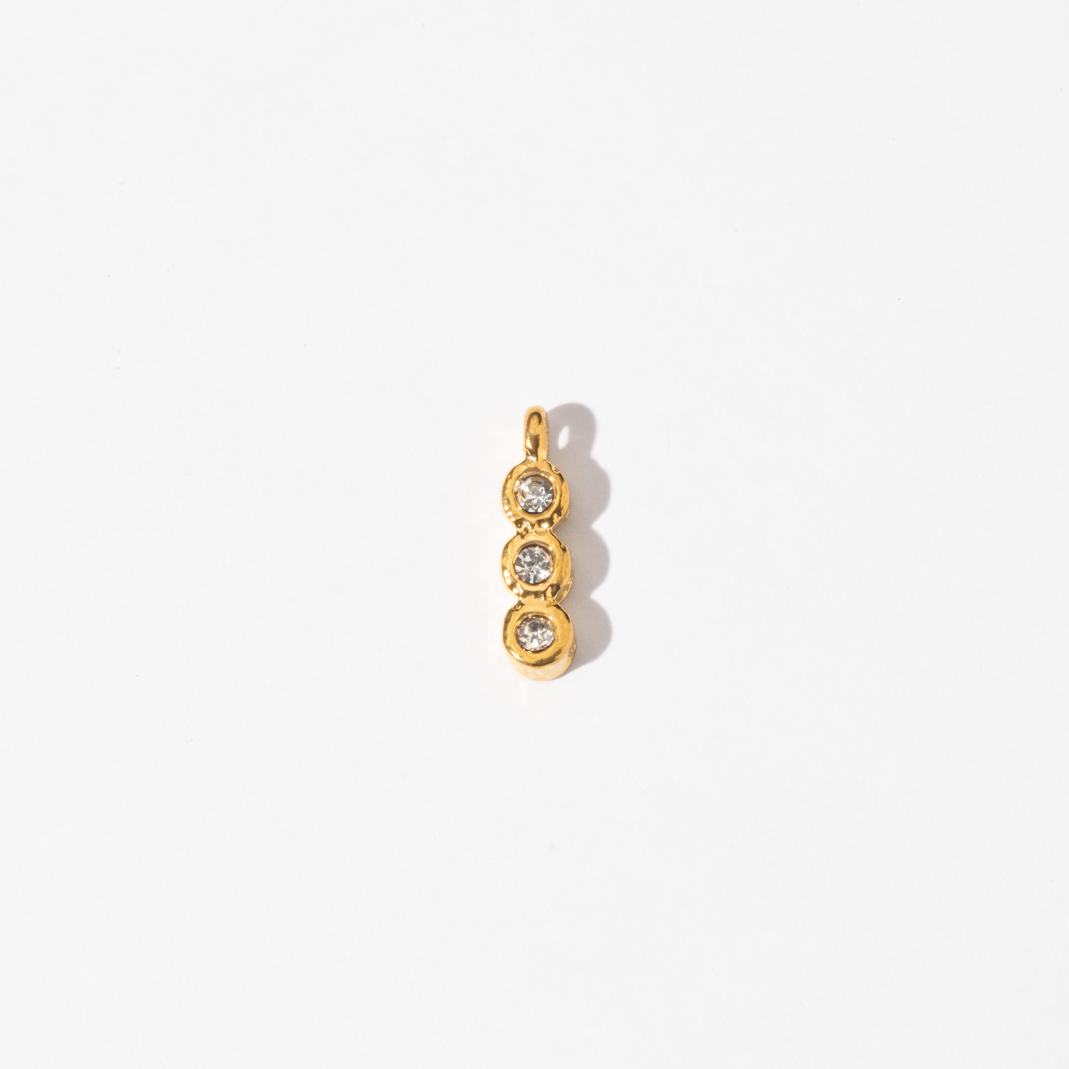 A gold-colored trinity charm with three circular designs containing two small white gems, intended for use with necklaces or bracelets.