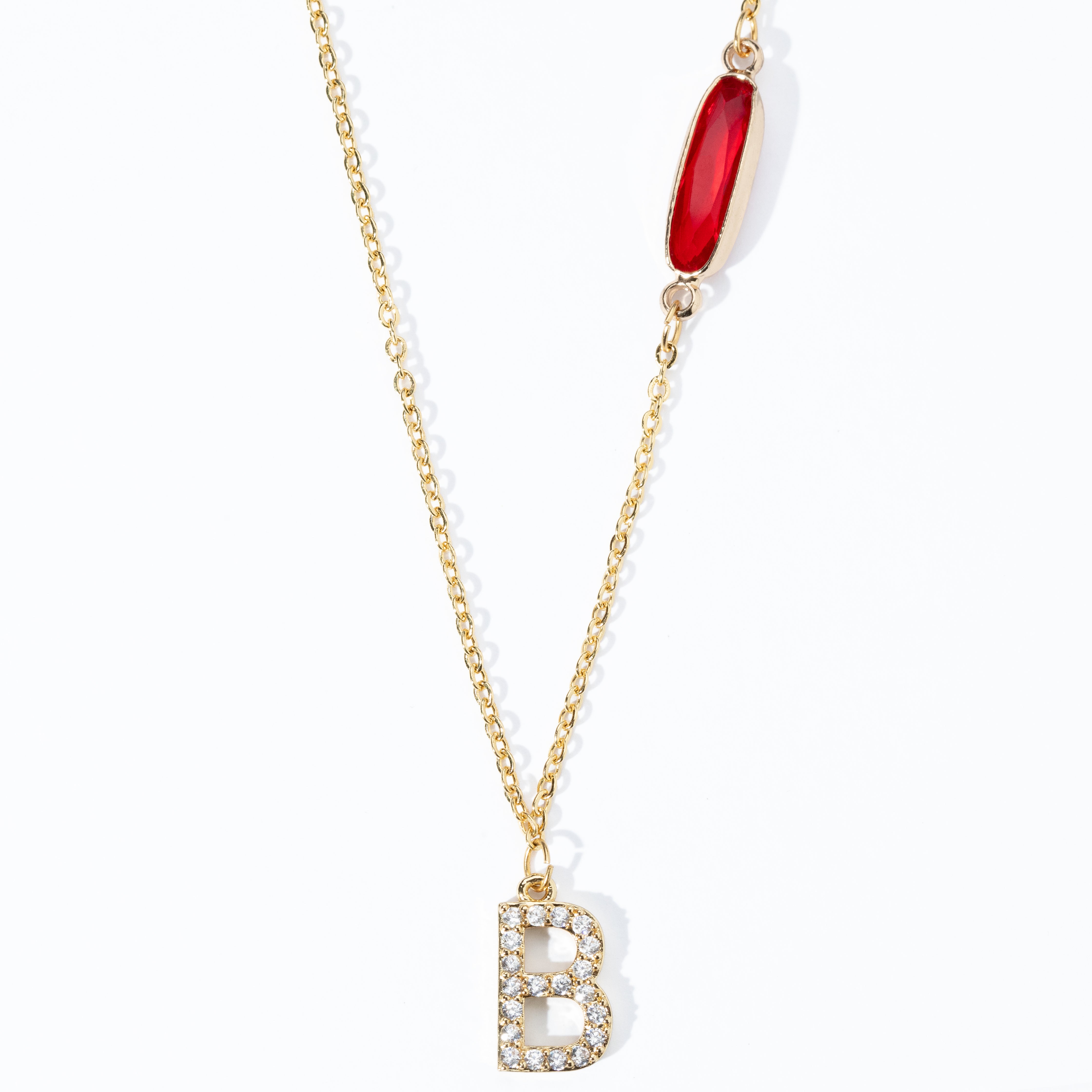 A custom gold-plated necklace with a diamond initial charm and a red birthstone pendant on a white background.