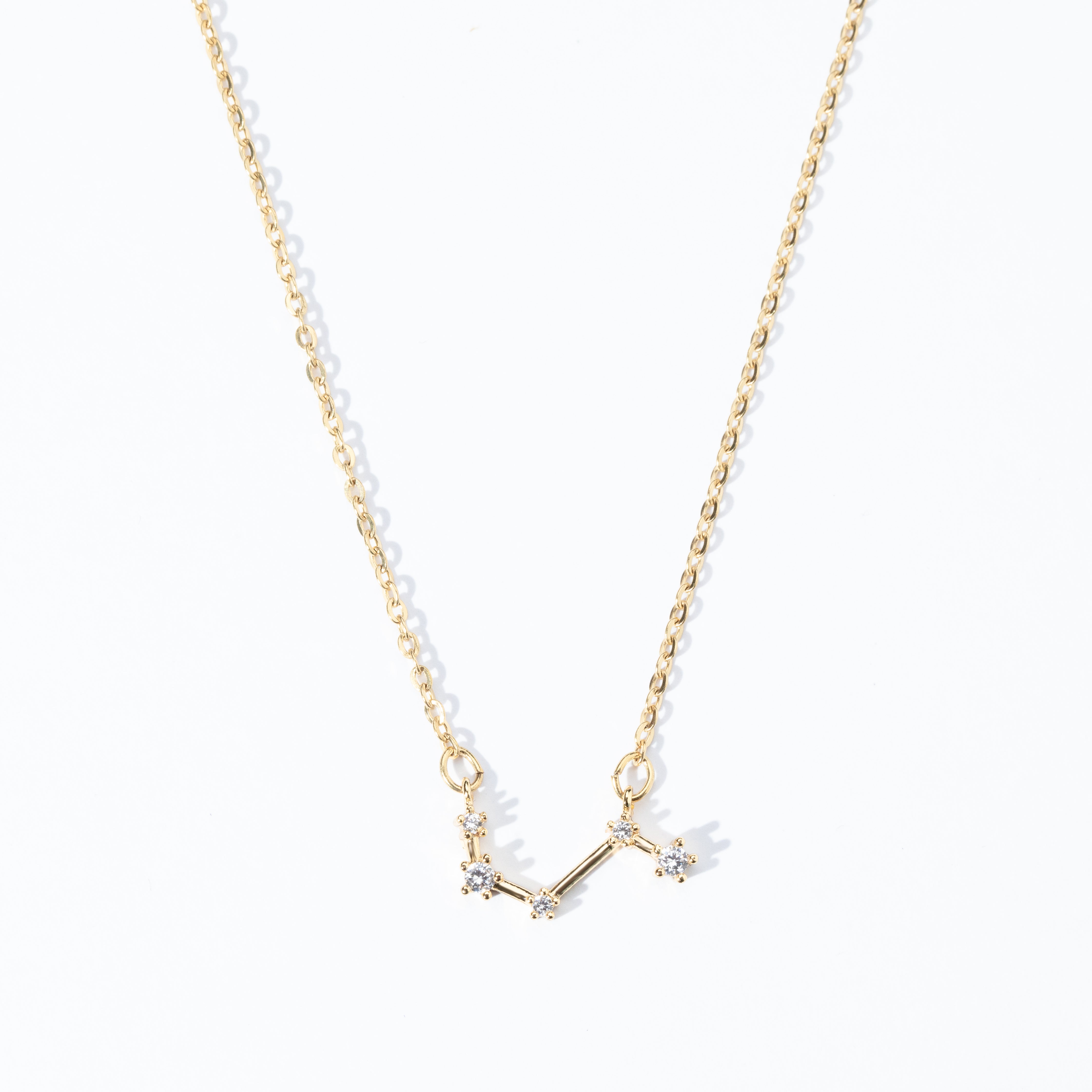 A dainty necklace with a gold chain and a charm featuring a zodiac constellation, adorned with small white crystals.