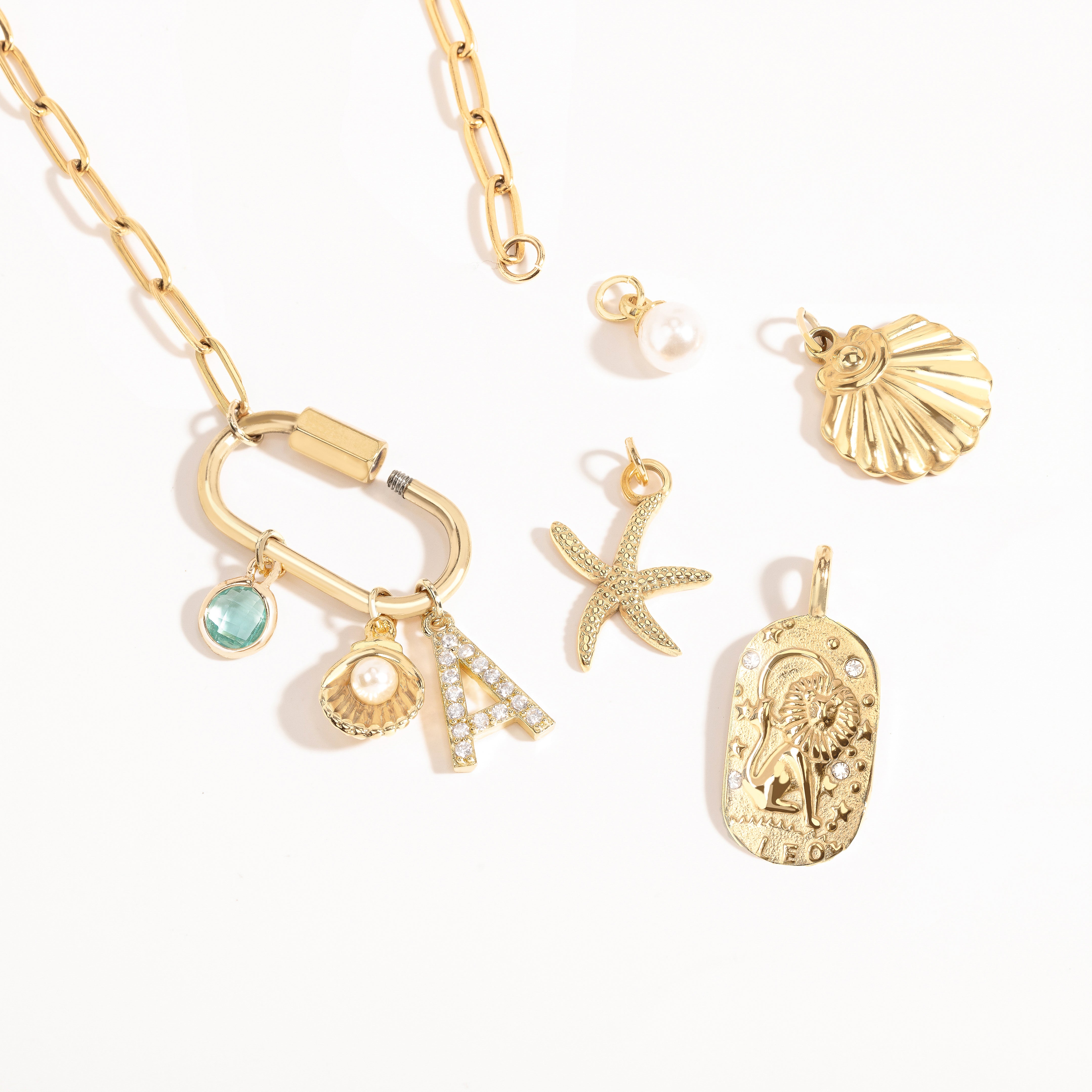 A Customize collection of gold-plated charms with travel-themed details, including a camera, suitcase, and airplane, accompanied by a gold chain and other small accessories.