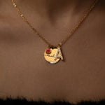 A gold necklace with a personalized initial and birthstone engraving.