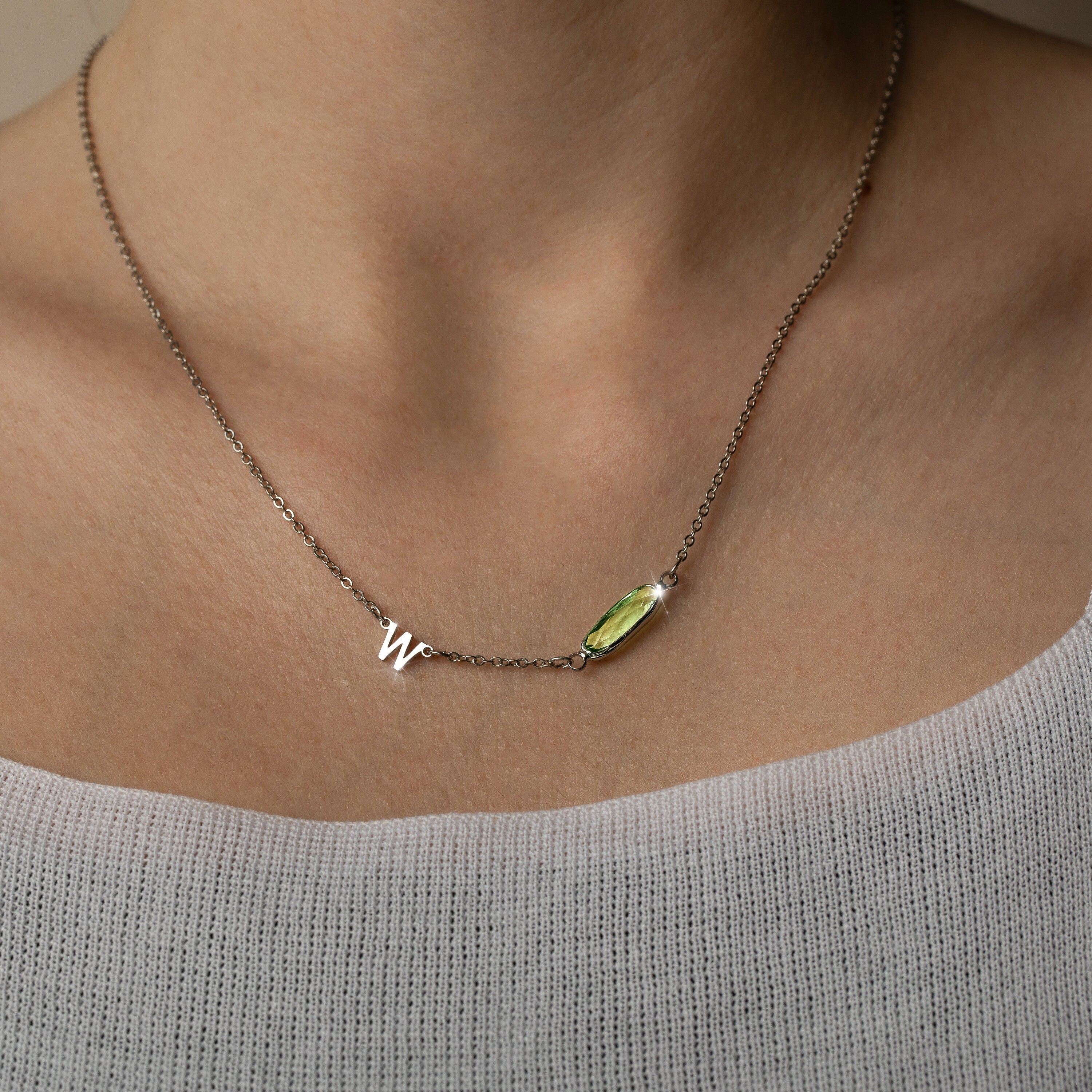 A necklace with a dainty chain and a delicate birthstone charm in the shape of an initial, displayed on a person.