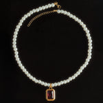 A pearl birthstone necklace with a gold-colored clasp and a purple birthstone pendant, displayed against a black background.