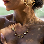 A woman wearing a gold-colored necklace with ocean-inspired charms such as seashells and starfish, and a personalized initial charm.