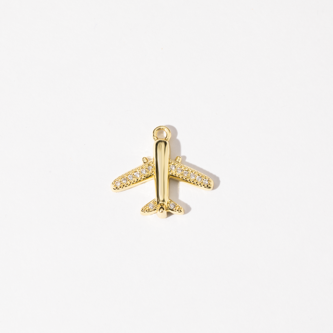 A gold-colored airplane-shaped charm with cubic zirconia stones adorning its body.