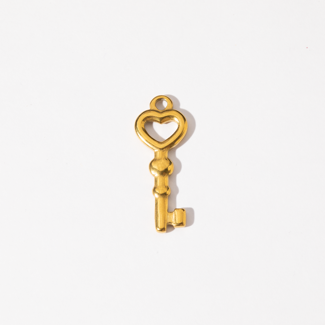 A gold-plated stainless steel charm in the shape of a key with a heart-shaped design at the top.