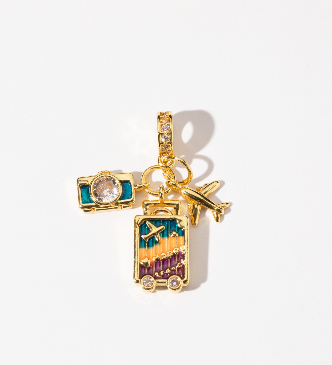 A gold-plated charm featuring detailed charms of a camera, suitcase, and airplane, adorned with vibrant cubic zirconia and sparkling accents.