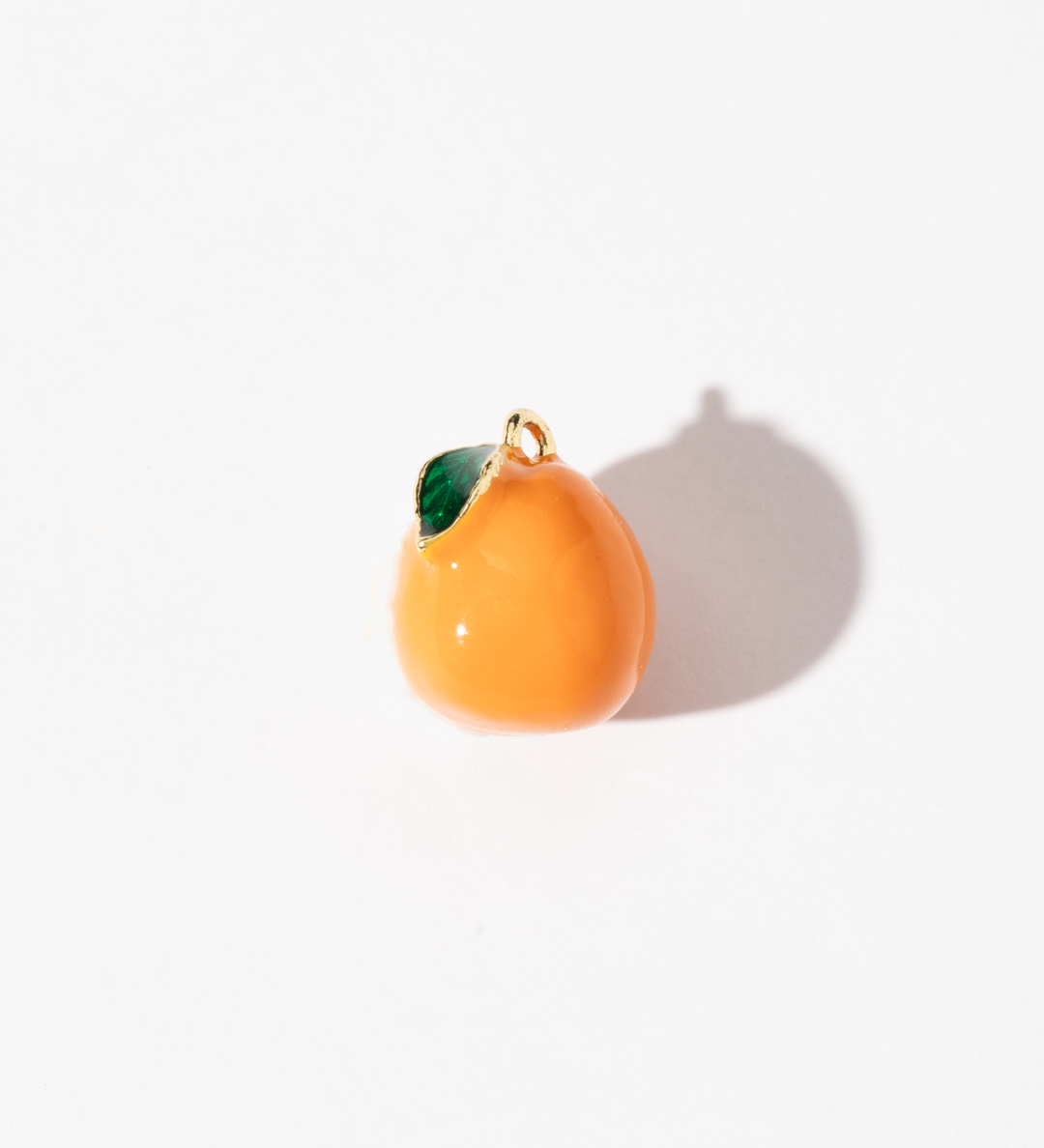 A gold-plated stainless steel charm in the shape of an orange with a green leaf detail, displayed against a white background.