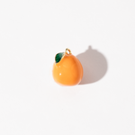 A gold-plated stainless steel charm in the shape of an orange with a green leaf detail, displayed against a white background.