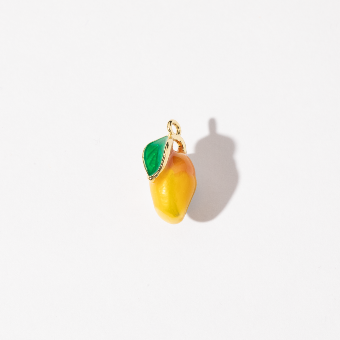 A gold-plated stainless steel charm in the shape of a mango with a green leaf, made with colored enamel.
