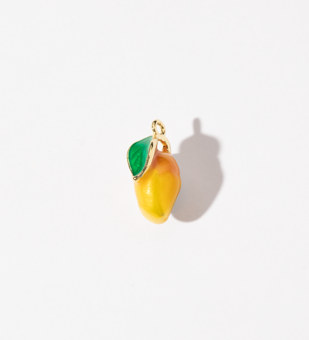 A gold-plated stainless steel charm in the shape of a mango with a green leaf, made with colored enamel.