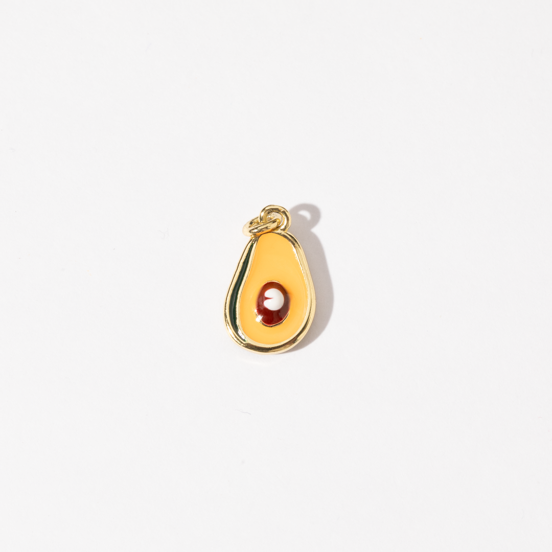 A gold-plated stainless steel charm in the shape of a half-avocado design with a polished seed at the center