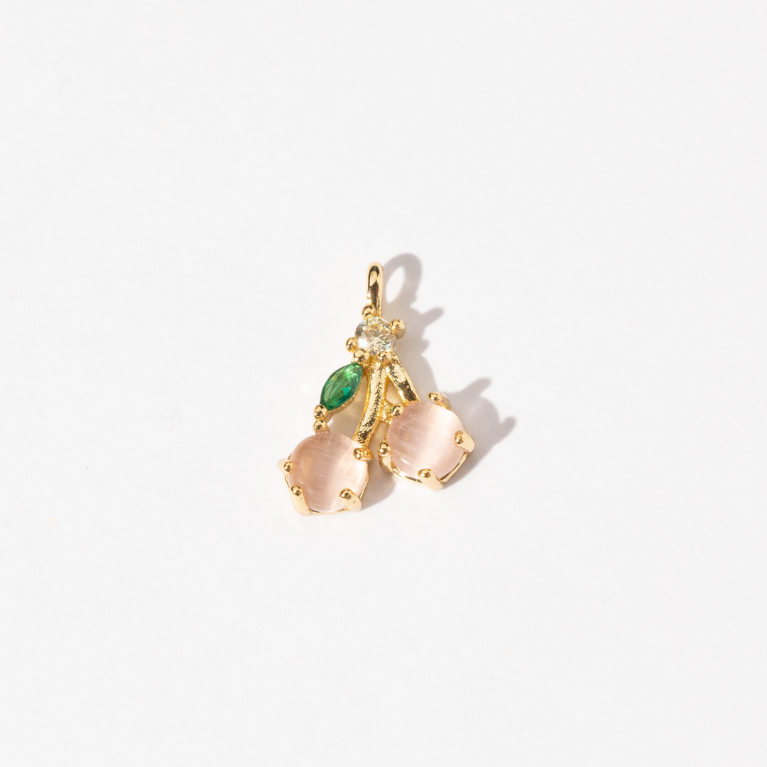 A gold-plated charm featuring a cherry design with pink stones and a small green gemstone accent.