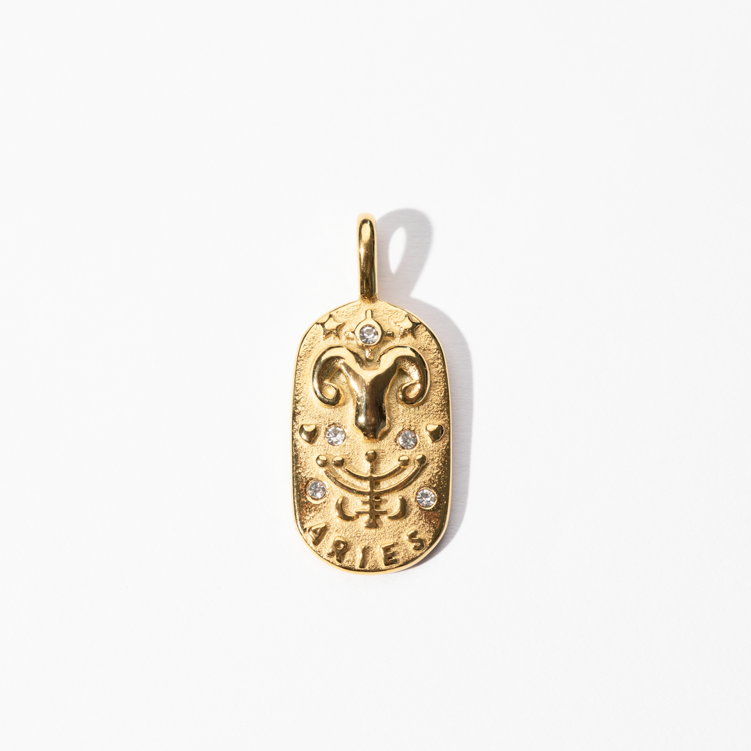 A gold-colored metal Aries medallion charm with intricate designs and small decorative stones.