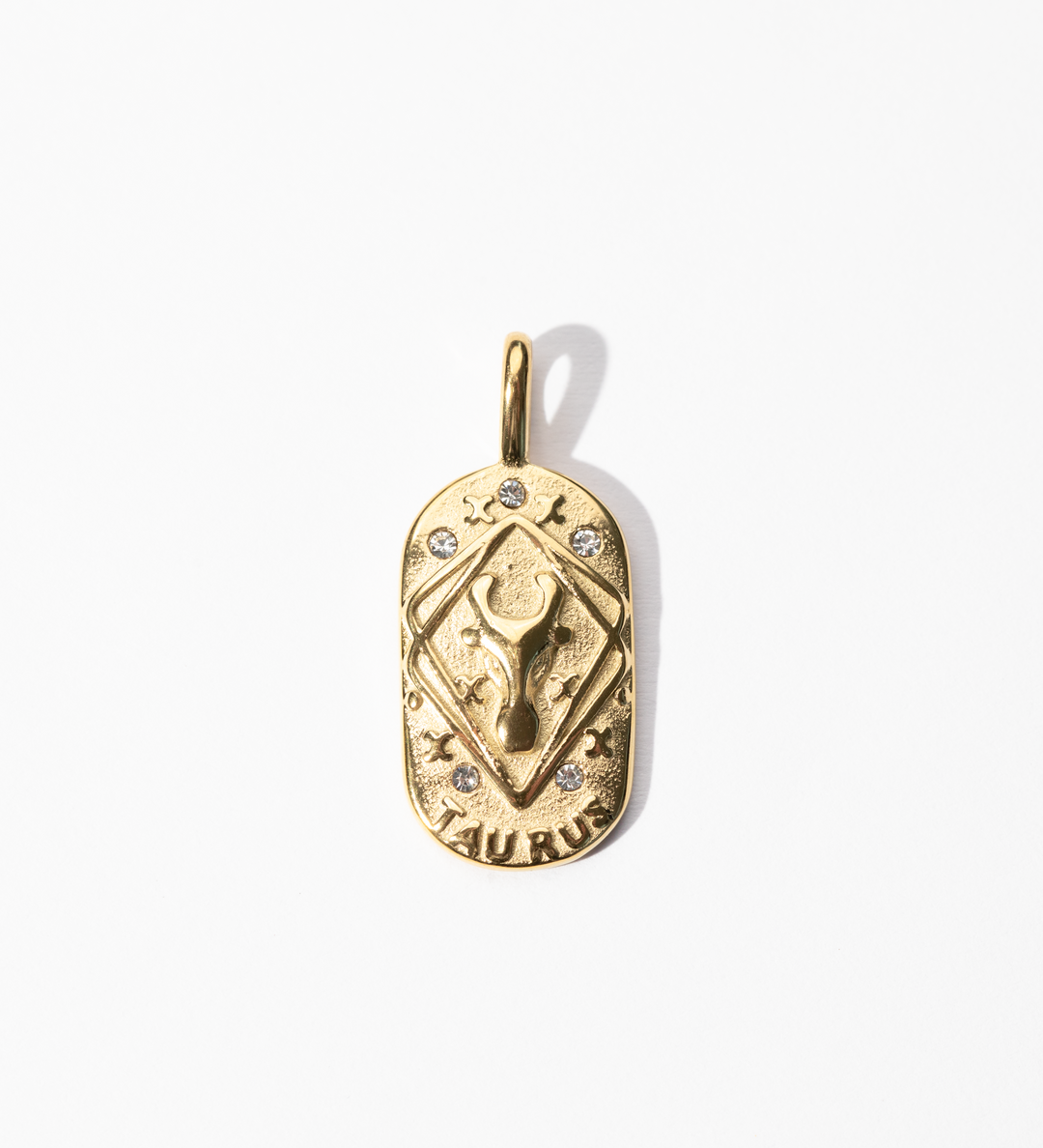 A gold-colored engravable Taurus medallion charm with intricate designs and small embellishments.