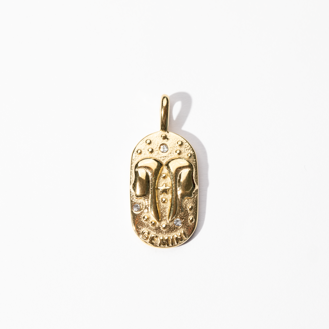 A gold-colored metal medallion charm with an engraved celestial design, symbolizing the zodiac sign Gemini.