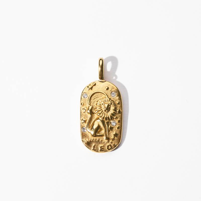 A gold-colored metal Leo medallion charm with intricate designs and small diamond-like embellishments.
