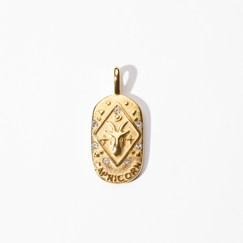 A gold-colored engravable Capricorn medallion charm with intricate design and small embellishments.