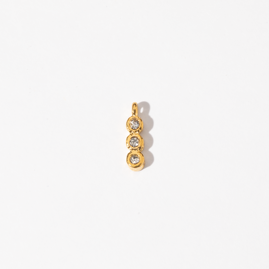 A gold-colored trinity charm with three circular designs containing two small white gems, intended for use with necklaces or bracelets.