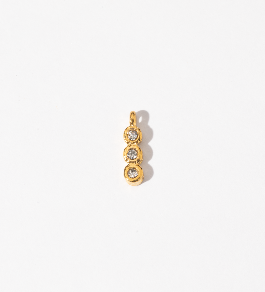 A gold-colored trinity charm with three circular designs containing two small white gems, intended for use with necklaces or bracelets.