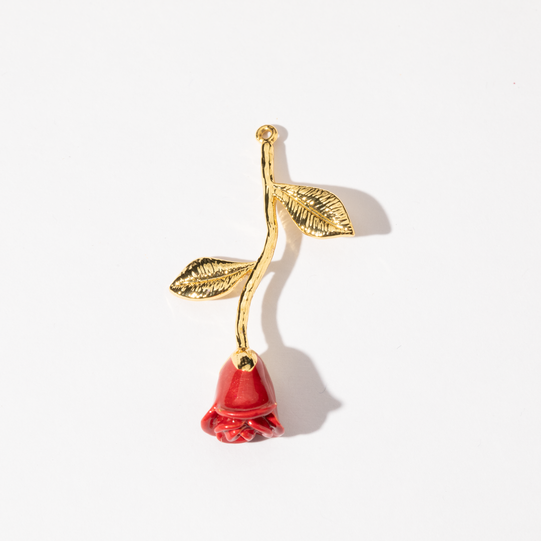 A gold-colored charm in the shape of a red rose with a leafy stem and a red flower.