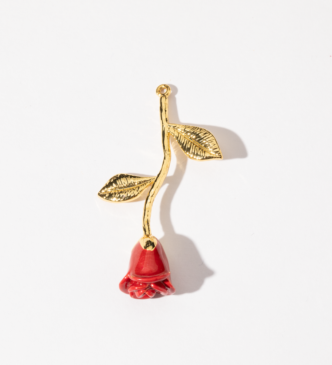 A gold-colored charm in the shape of a red rose with a leafy stem and a red flower.