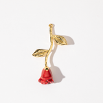 A gold-colored charm in the shape of a red rose with a leafy stem and a red flower.