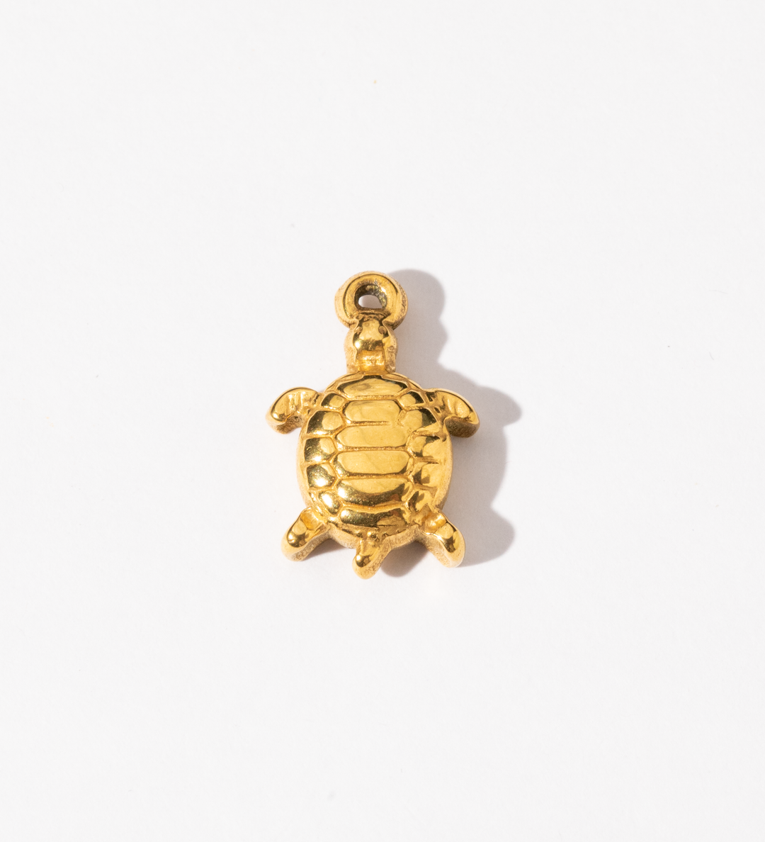 A gold-colored stainless steel turtle charm against a white background.