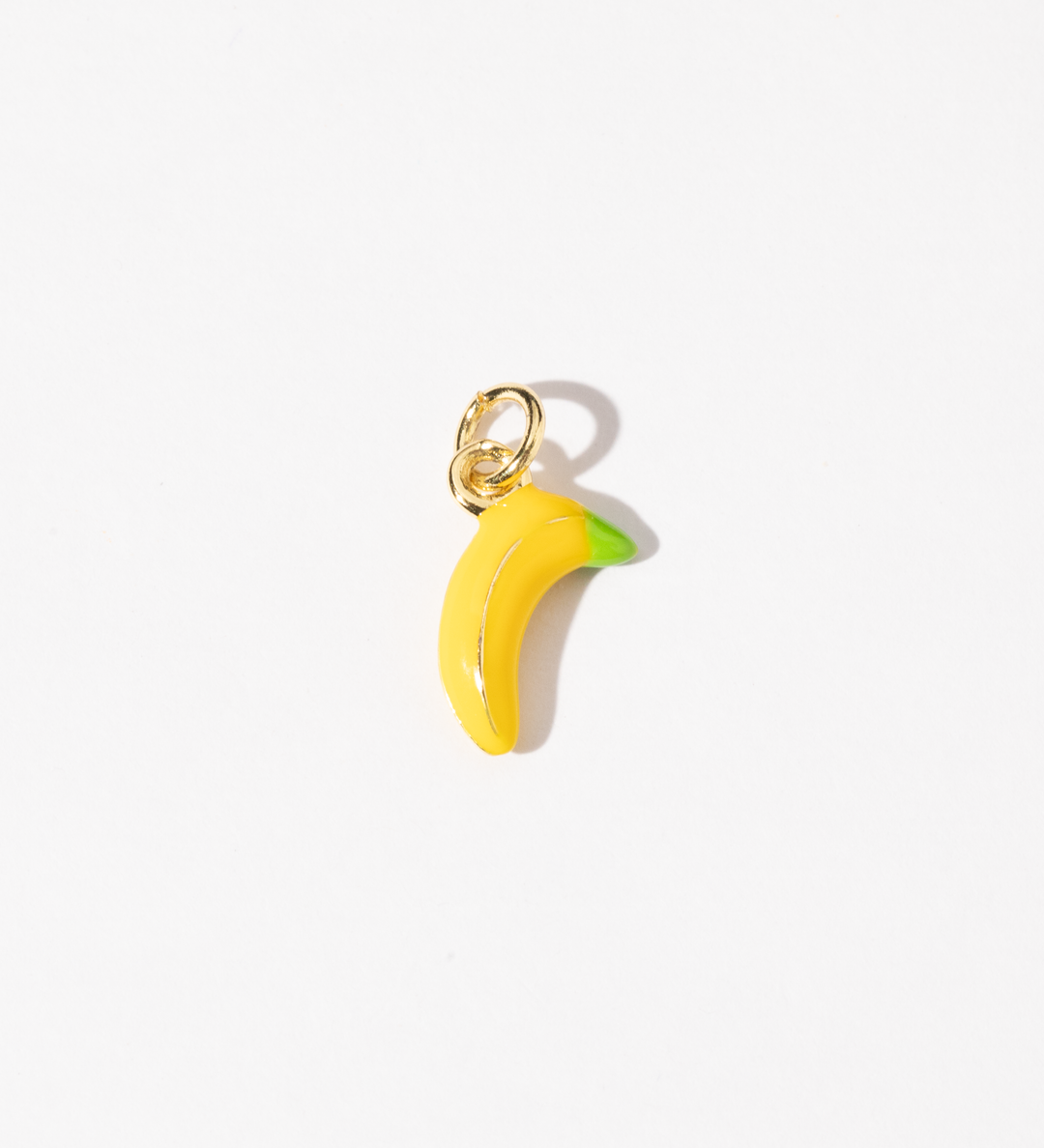 A gold plated stainless steel charm in the shape of a banana with yellow and green tones.