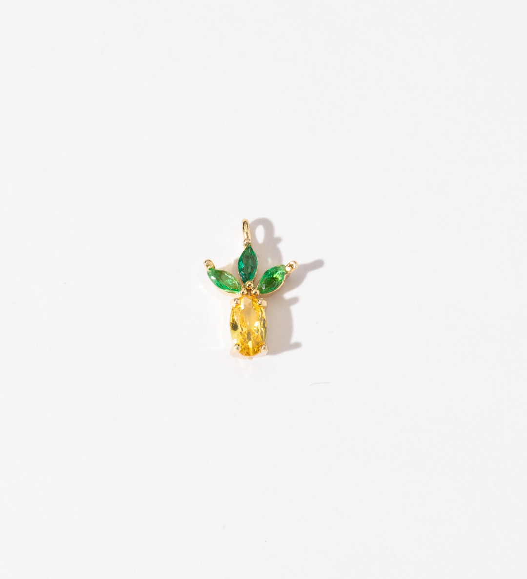 A gold plated stainless steel charm featuring a personalizing of yellow faceted zirconia in the shape of a pineapple with green marquise-cut stones as leaves on a white background.