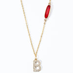 A custom gold-plated necklace with a diamond initial charm and a red birthstone pendant on a white background.