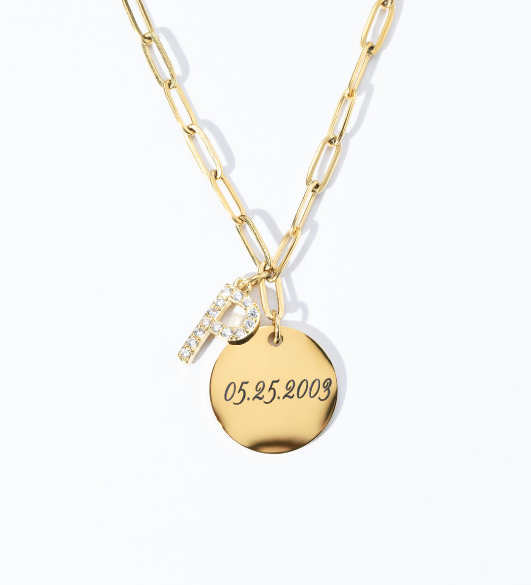 A gold paperclip chain necklace with a gold coin charm personalized with text and a pavé initial.