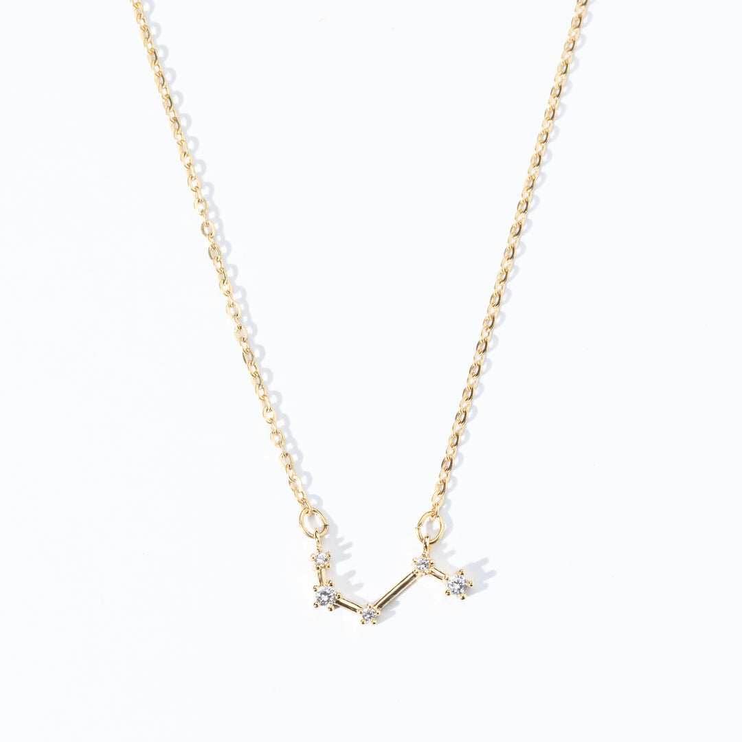 A dainty necklace with a gold chain and a charm featuring a zodiac constellation, adorned with small white crystals.