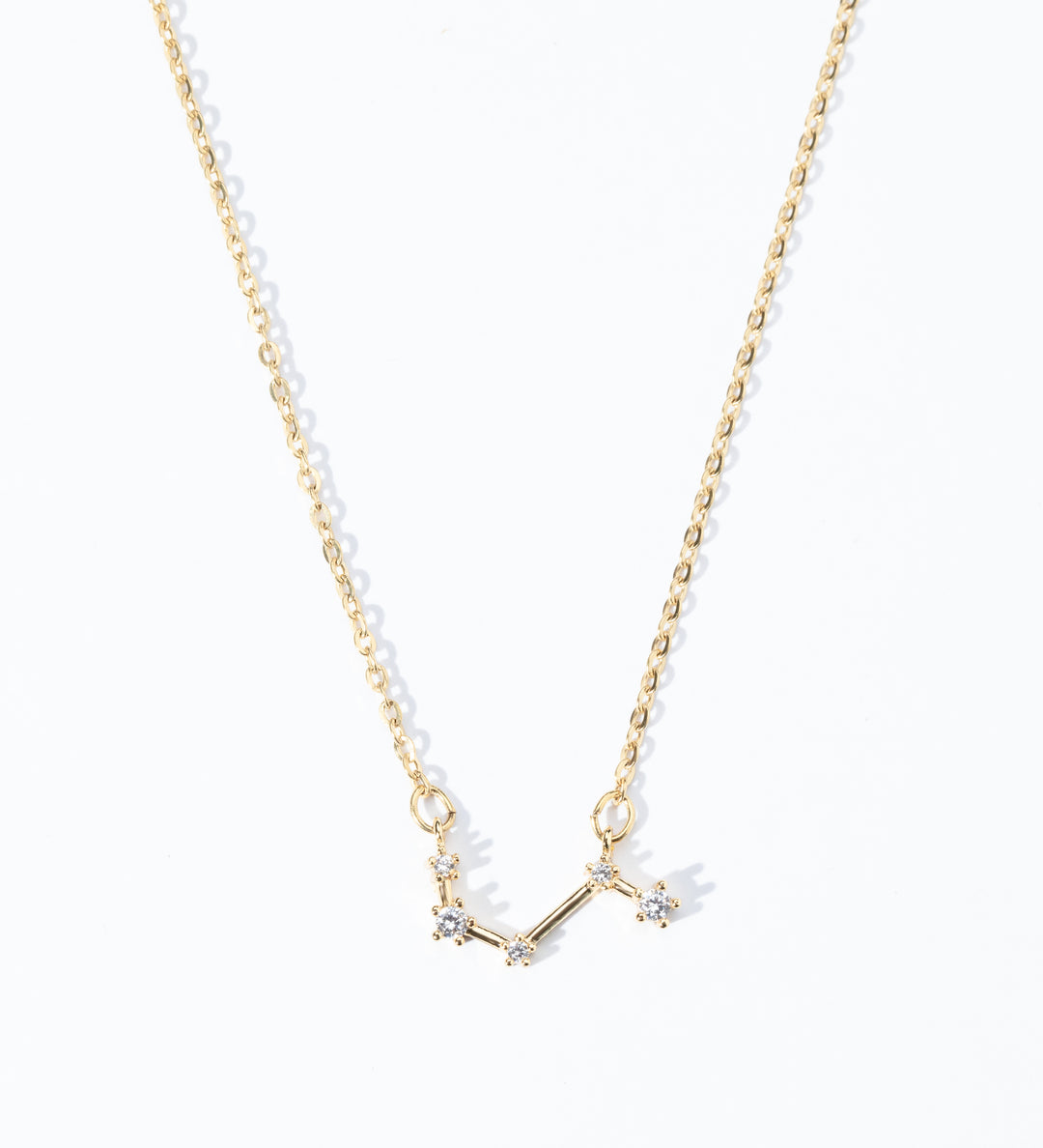 A dainty necklace with a gold chain and a charm featuring a zodiac constellation, adorned with small white crystals.