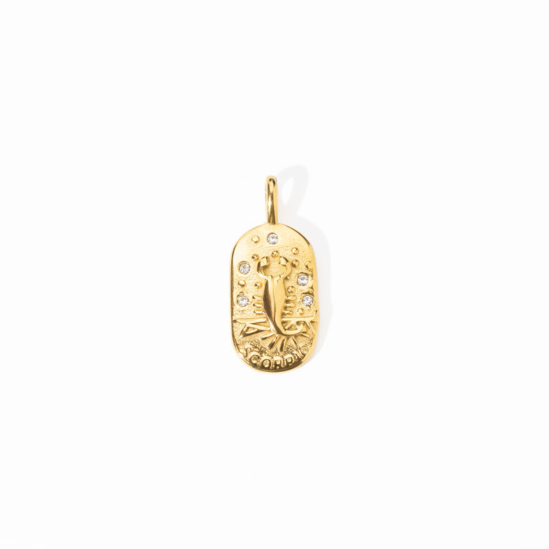 A gold-colored engravable Scorpio medallion charm with intricate designs and small embedded stones.