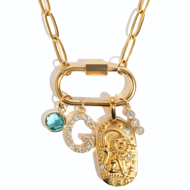 A gold-colored personlized carabiner necklace base with a link chain, a large carabiner clip, and three charms attached: a blue birthstone, a 'G' initial, and a gold-tone charm with intricate design.
