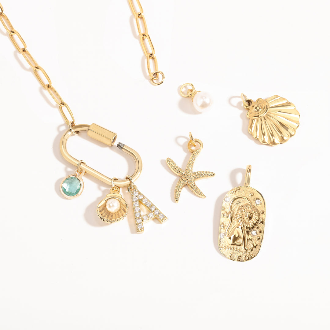 A Customize collection of gold-plated charms with travel-themed details, including a camera, suitcase, and airplane, accompanied by a gold chain and other small accessories.
