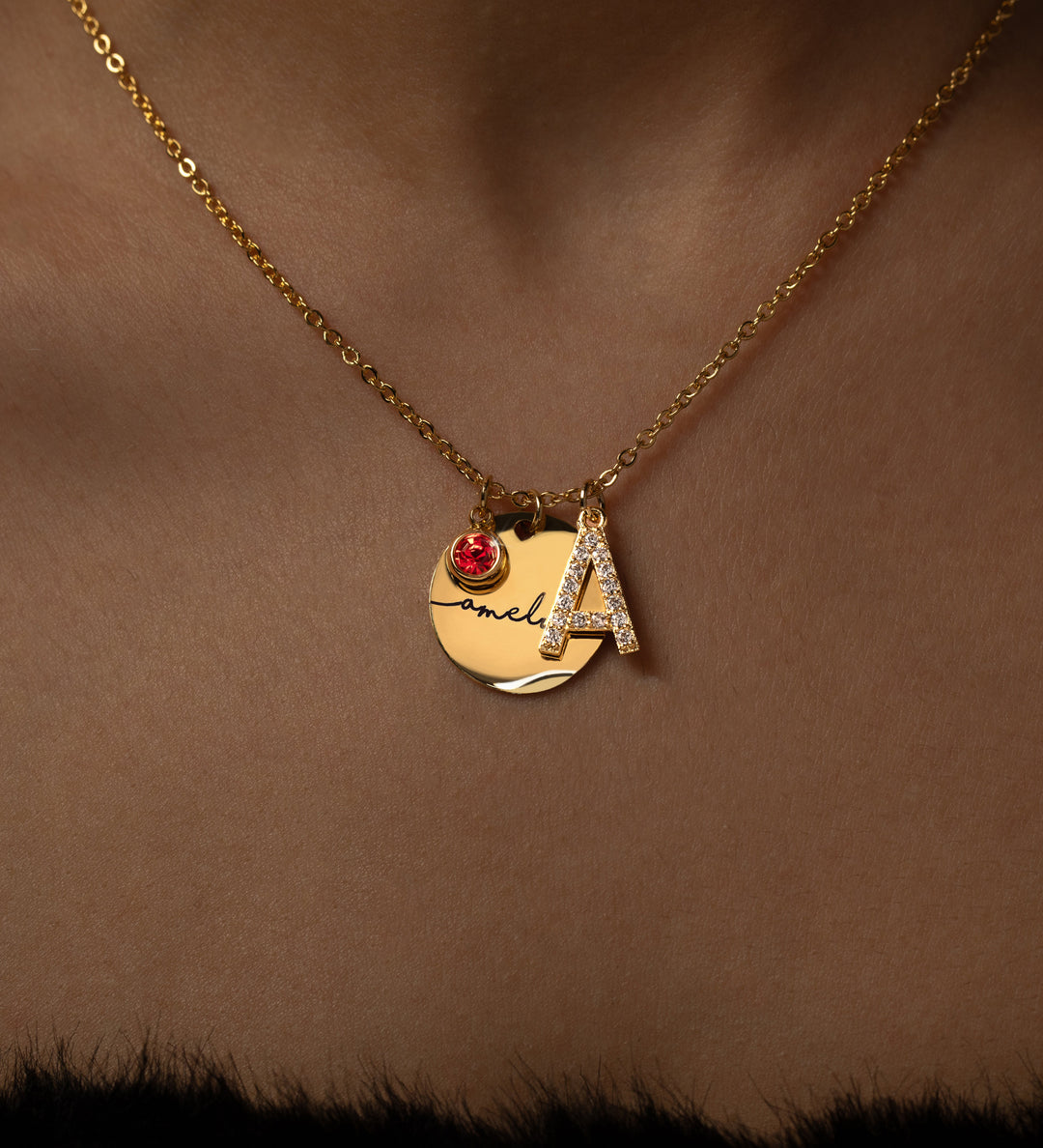 A gold necklace with a personalized initial and birthstone engraving.