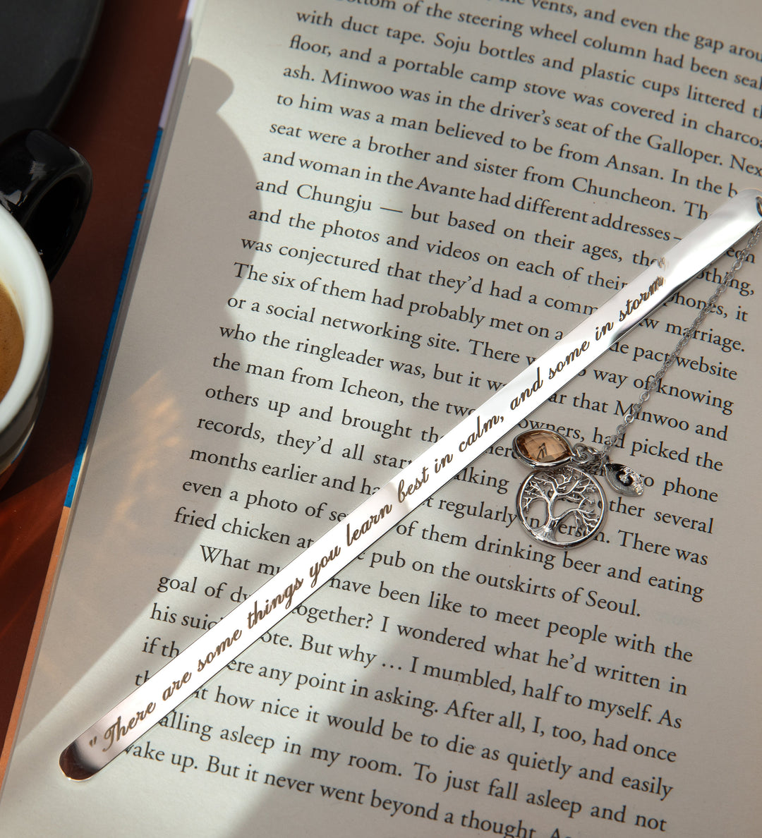 A personalized metal bookmark with a custom birthstone, an engraved initial leaf, and a Tree of Life pendant, displayed on an open book.