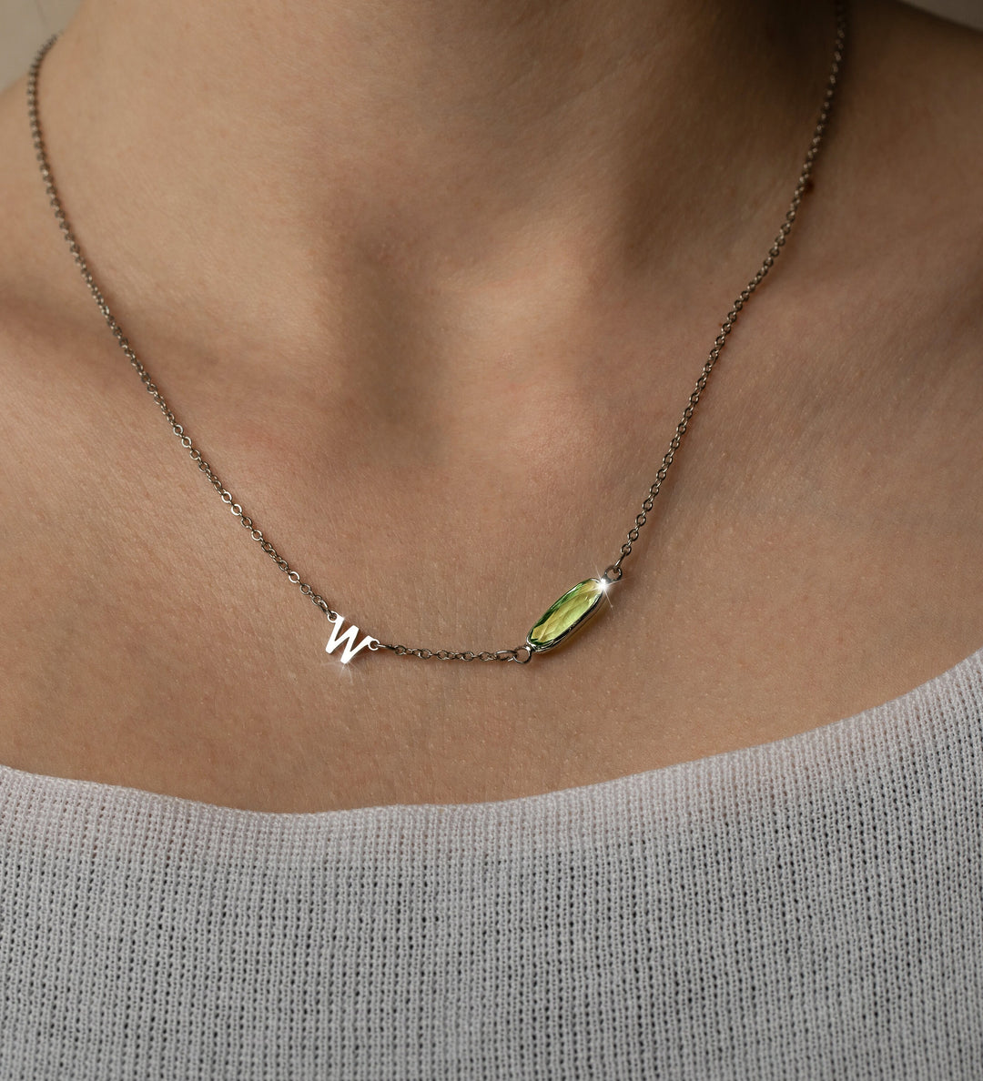 A necklace with a dainty chain and a delicate birthstone charm in the shape of an initial, displayed on a person.