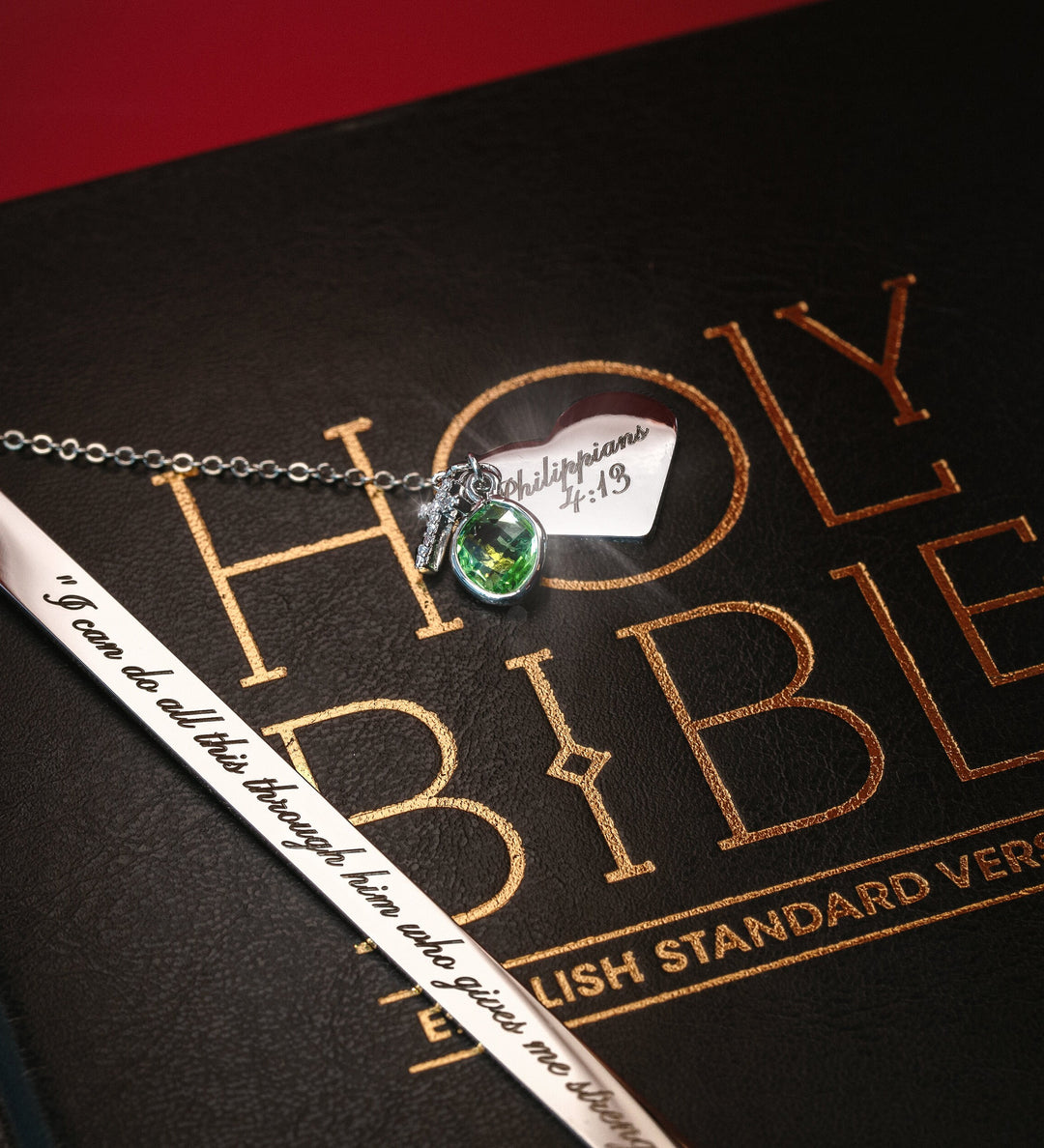 A personalized Bible bookmark with a heart-shaped charm and a metal chain, placed on an open Bible with a note 'I have become all things to all people' written on it.