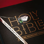 A personalized Bible bookmark with a heart-shaped charm and a metal chain, placed on an open Bible with a note 'I have become all things to all people' written on it.