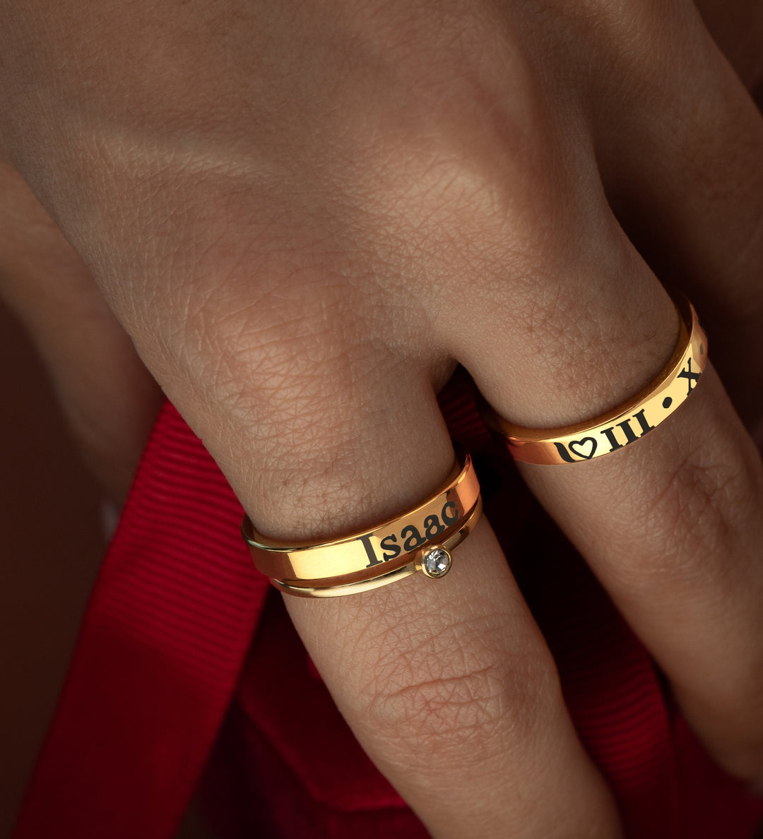 A close-up image of a person's hand wearing two gold-colored rings with engraved text on each.