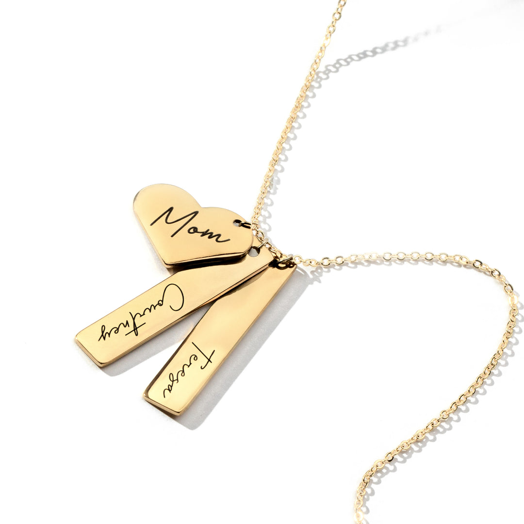 A gold-plated necklace with a vertical heart cutout charm and two engraved bars on a cable chain.